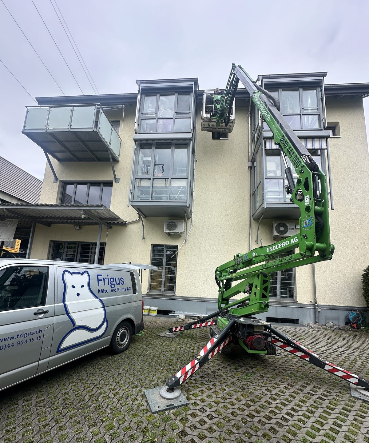 Frigus-Servicefahrzeug mit Fuchs-Logo vor einem Gebäude, davor eine Hubarbeitsbühne